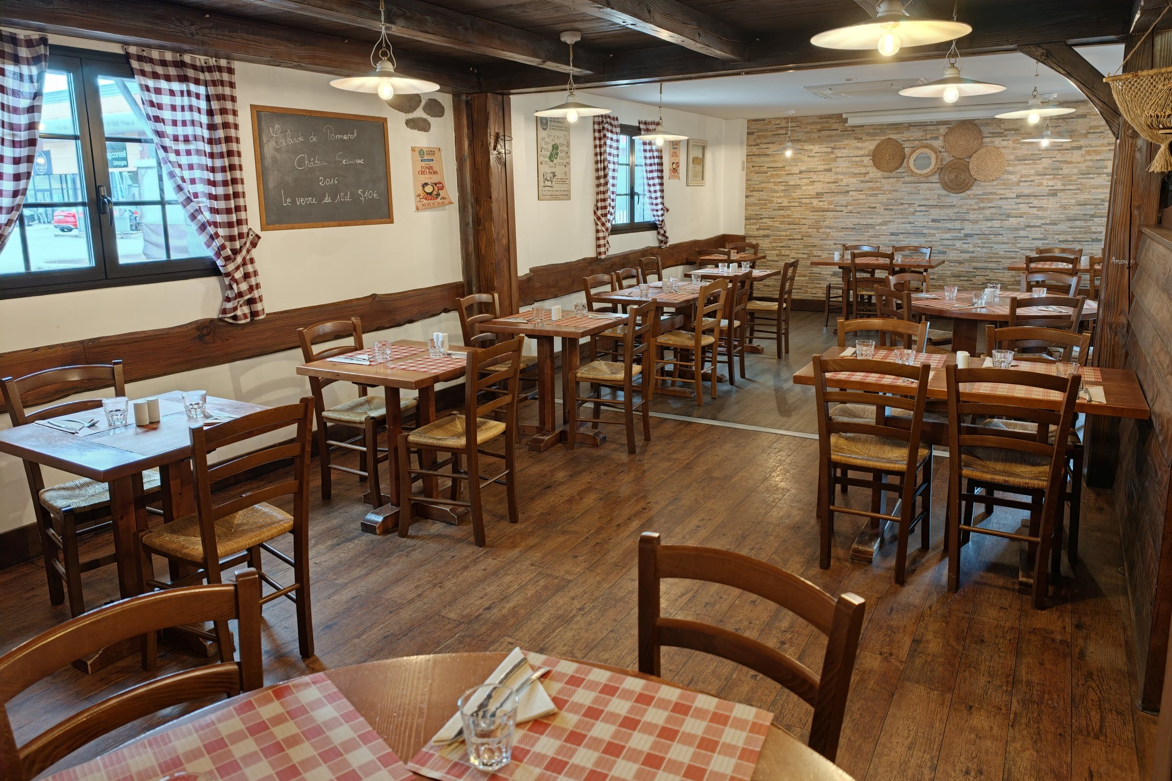 Une salle du restaurant dressée, tables en bois et nappes à carreaux