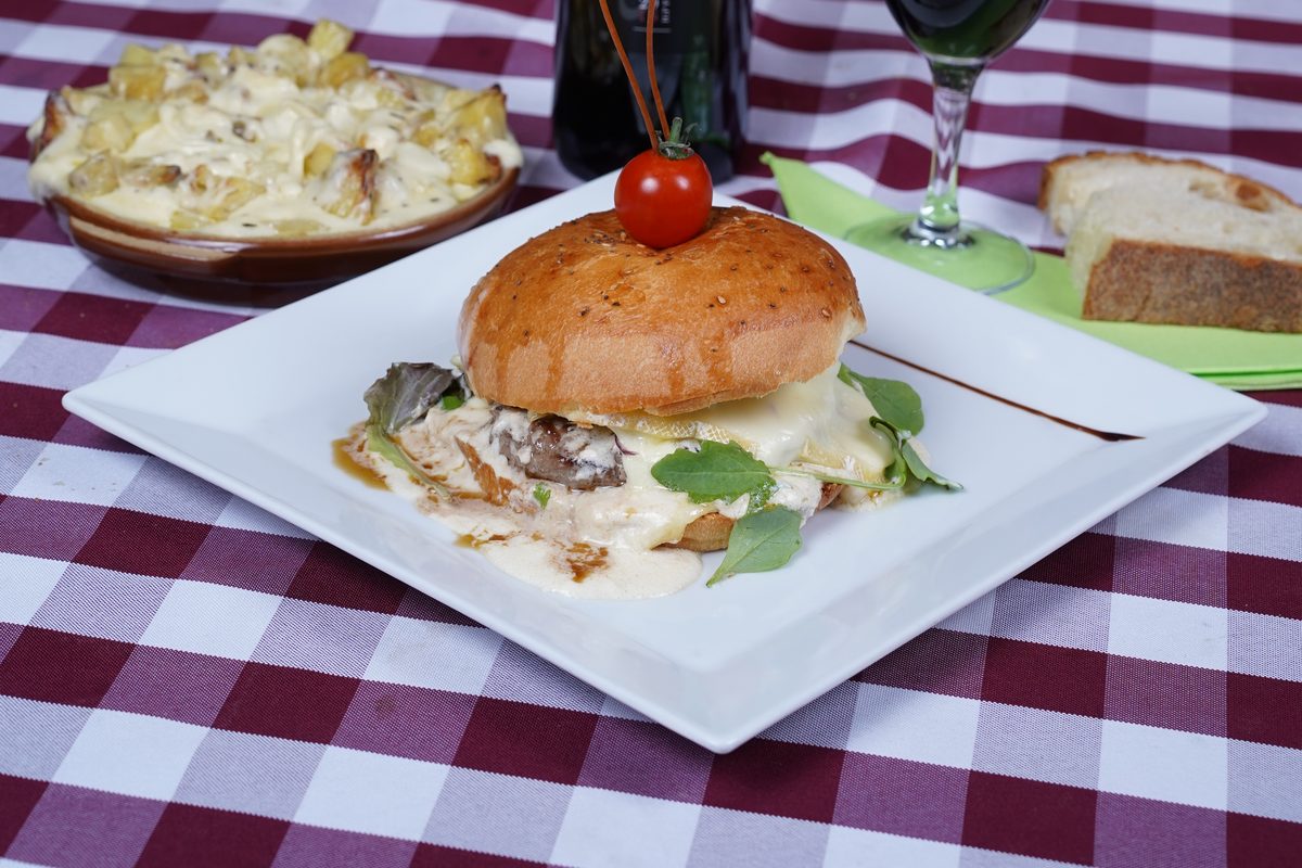 Un burger de la carte nappé de fromage fondu, servi sur une assiette blanche avec un verre de vin