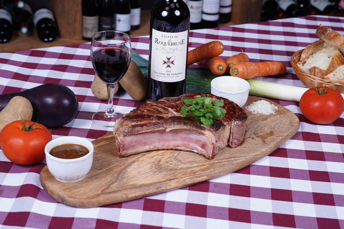 A grilled rib of Limousin beef on a wooden board, with vegetables, bread and a homemade sauce