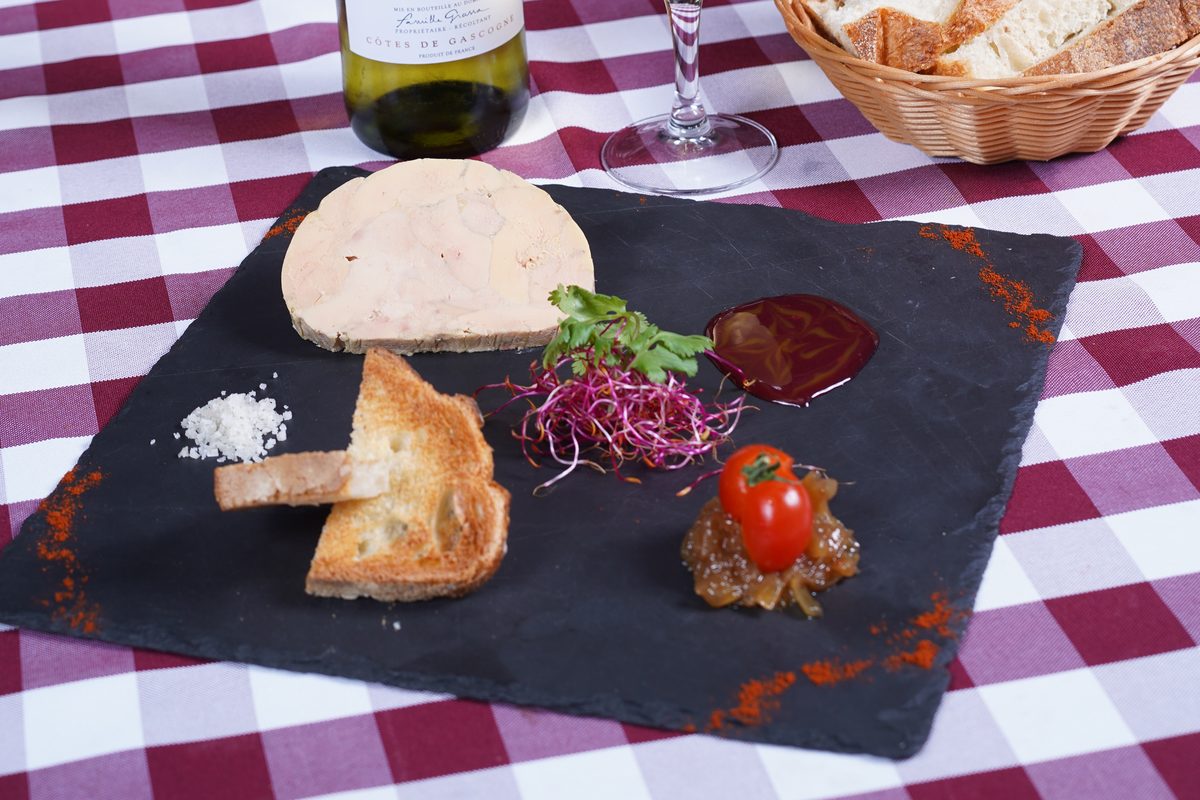 Une tranche de foie gras sur une ardoise, avec du pain grillé, un chutney et une tomate cerise