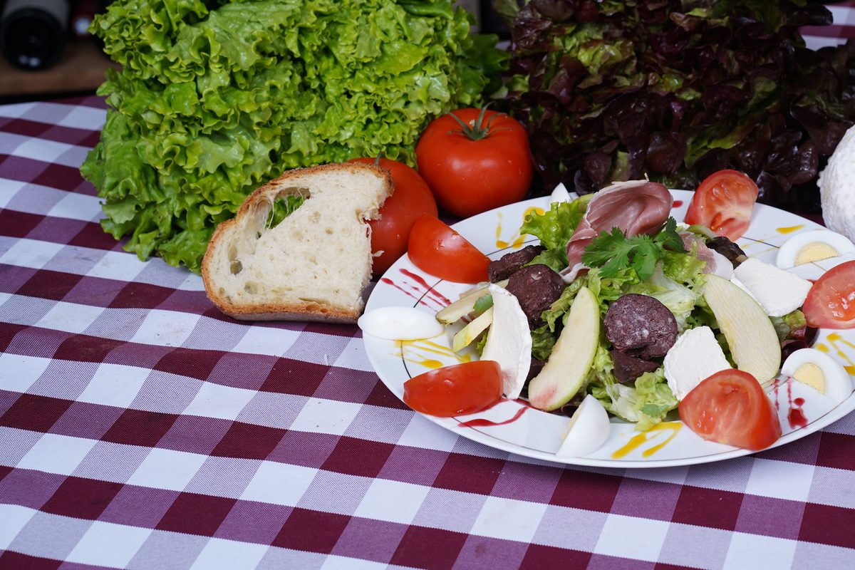 Une salade composée avec des œufs durs, du fromage, des tomates et du pain, devant des salades entières
