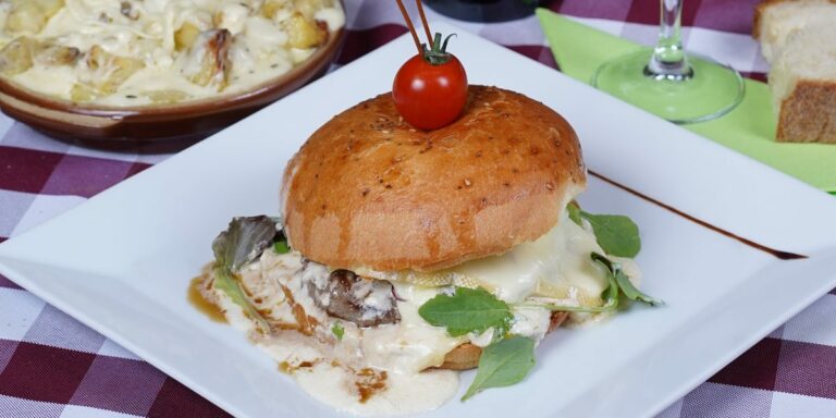 Un burger de la carte, pain doré et fromage fondu, servi sur une assiette blanche Au Paysan Gourmand